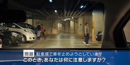 実写版 危険予知「SCENE42　駐車場編 その2 駐車場で車を止めようと空いているスペースを探しています。右側には女性、左前方には男女のカップルが歩いています。