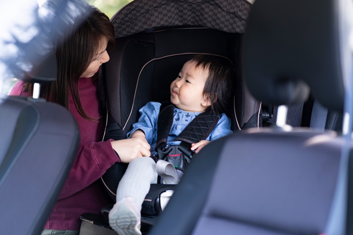 チャイルドシートに座る幼児を見つめる母親